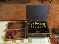 Wooden box with hinged lid open showing custom ceramic chess pieces arranged in compartments and foldable wooden checkerboard with black and red checkers on adjacent surface.