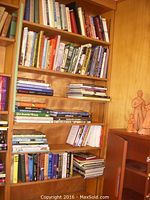 Full bookshelf of hardcover books, varied subjects and sizes, arranged on wooden shelving with a small Native girl head vase on right.