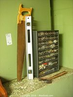 Hardware cabinet, hand saw, spirit level, and crowbar against green wall on granite surface