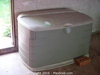 Full left-side angled view of the beige/tan Rubbermaid outdoor storage container showing overall shape and dimensions.