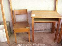 Wooden child's school desk with matching chair side by side against a wall showing the desk's and chair's wear and natural wood finish.