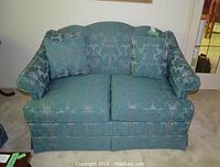 Full frontal view of a Thomasville upholstered love seat with two accent pillows and arm covers in patterned blue-green fabric.