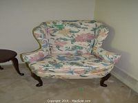 Full view of the floral wing chair upholstery and front wooden carved legs.