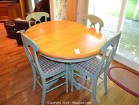 Round wood top table on green pedestal base with four chairs arranged around it