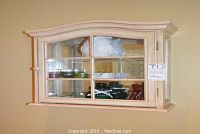 Front view of the cream-colored wooden wall cabinet with glass door and visible decor inside.