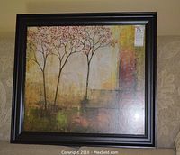 Framed print showing an abstract painting of three thin trees with reddish leaves against textured earth-tone background.