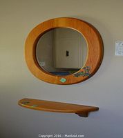 Wooden hanging oval wall mirror with natural finish and floral detail, matching curved wooden shelf mounted below