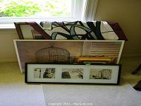 Group photo of the four framed prints and fabric wall hanging stacked by a window on carpeted floor.