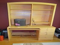 Light-colored wooden desk and bookcase unit with multiple shelves and drawers, showing a paper shredder placed on the desktop shelf.