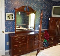 Photo of Thomasville wooden dresser with attached large mirror, showing nine drawers and central cabinet, dark wood finish, brass hardware, situated in floral wallpaper room.