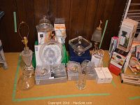 Full view of lot showing multiple boxed and unboxed glassware including bowls, cheese dome, cut glass lamp base, and small table lamp.