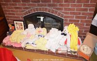 Wide shot of assorted baby clothes in various pastel colors displayed on fireplace hearth, includes booties and blankets