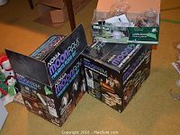 Two black boxes of Noma Moon Rays outdoor lights and one green box of Emerald solar garden lights shown unopened and with contents visible