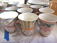 Eight assorted hand-painted ceramic coffee mugs on fabric surface