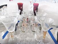 Photo showing eight champagne glasses with floral paint and gilt, two cranberry glass flutes with heart motifs, and seven large air bubble wine glasses.