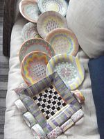 Eight round hand-painted plates arranged on sofa with napkin rings and square tray