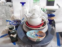 Shows entire lot from above including large ceramic tray, teapot, plates, bowls, glass containers, Harrods salt and pepper shakers, and cobalt Venetian glass goblet