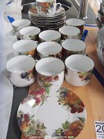 Top view of twelve porcelain cups and saucers stacked and arranged on a wooden surface, showing fruit and berry decorations.