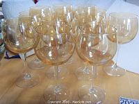 13 tall wine glasses with pale amber bowls and clear stems arranged on table.