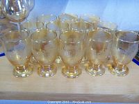 Twelve amber-colored etched water glasses shown together in two rows, highlighting the footed bases and floral etched designs.