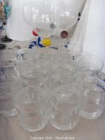 Group photo showing eleven clear rock glasses with geometric etching in front and four decorative wine glasses with colored spheres on stems in the background.