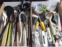 Two boxes filled with a wide assortment of kitchen utensils, including spatulas, serving spoons, forks, whisks, potato peelers, can openers, and wooden utensils with a variety of handles and materials