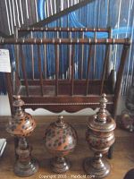 Wooden magazine rack with two long turned spindle handles and scalloped base, set behind three turned wood lidded urns with spotted patterns and dark finish.