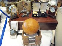 Two miniature Roger Lascelles mantel clocks, Timex wristwatch, small globe, and metallic figurine arranged on a wooden box