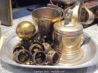 Nambe white metal tray holding a globe-shaped inkwell, metal trinket box with lion finial, metal bucket, and a cluster of bronze-tone ornate napkin rings.