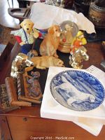View of assorted dog figurines, brass bookends, golden retriever figurines, and snow globe music box arranged on a wooden surface.