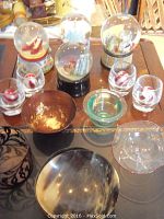 Overview of the lot showing four snow globe music boxes, four glass votive candleholders with red cherry designs, and five decorative bowls in various materials and colors.