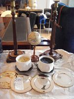 Two tall wooden candlesticks, two white Muse bisque candleholders on black metal bases with original candles, four silver-plated round dishes, and a decorative Earth globe on wooden stand.
