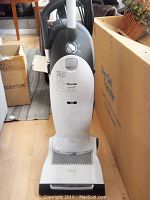 Front view of Miele vacuum cleaner, showing body and base, white with black bottom section.