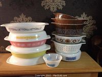 Comprehensive view of all dishes stacked on a wooden surface showing mix of Pyrex, Hazel Atlas, and Fire King glassware.