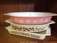 Stacked view of 3 Pyrex baking dishes showing pink oval divided dish on top with white flowers, and two rectangular dishes below with brown floral/vine patterns
