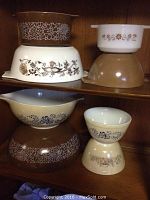 Shelf with stacked brown and white Pyrex bowls with floral patterns and a Termocrisa bowl on top