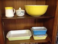 Full view of six pieces of Pyrex including mixing bowl, baking dish, two storage containers with lids, sugar dish with lid, and unmarked mug.