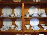 Full view of multiple shelves displaying the Blue Delphite dinnerware including plates, cups, and bowls arranged in groups.