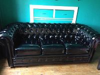 Front view of black vinyl tufted couch showing seat cushions and storage drawers beneath.