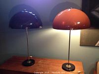 Pair of vintage table lamps placed on wooden surface against blue wall, both lamps with brown plastic dome-shaped shades and metal stems and bases.
