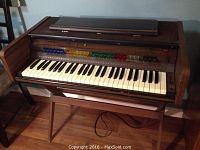 Front view of the Lowrey Wandering Genie L-2 organ with the wooden stand and visible keyboard and preset buttons.