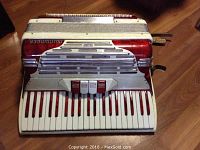 Front view of the Mundinger accordion showing piano keys, switches and red-white finish.