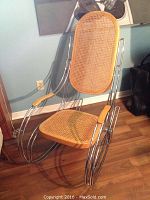 Front view of mid century modern rocking chair showing cane seat, backrest and metal tubular frame with curved rockers.