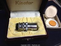 Kinotar branded box containing the chrome metal 6mm f1.9 wide angle lens resting on yellow padded fabric.