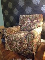 Full view of the floral upholstered armchair against wallpapered wall