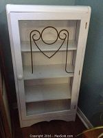 Full view of the white wooden cabinet with glass front door and decorative metal design on the glass.