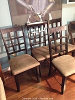 Photo showing four wooden dining chairs with dark finished lattice backs and light brown upholstered seats, placed on wooden floor.