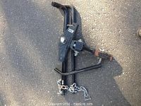 Black Robin weight distributing trailer hitch assembled with hitch ball and chains laid on asphalt.