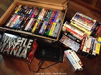 Wooden box opened showing assortment of VHS tapes arranged front facing the viewer, titles visible including dramas and action films.