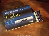 Boxed Electrohome DVD player EH 8181A with several DVDs stacked beside it on a wooden floor.